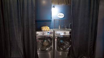 A laundry area with two front-loading washing machines, a drying rack, and a sign indicating a laundry service.