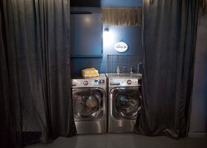 A laundry area with two front-loading washing machines, a drying rack, and a sign indicating a laundry service.