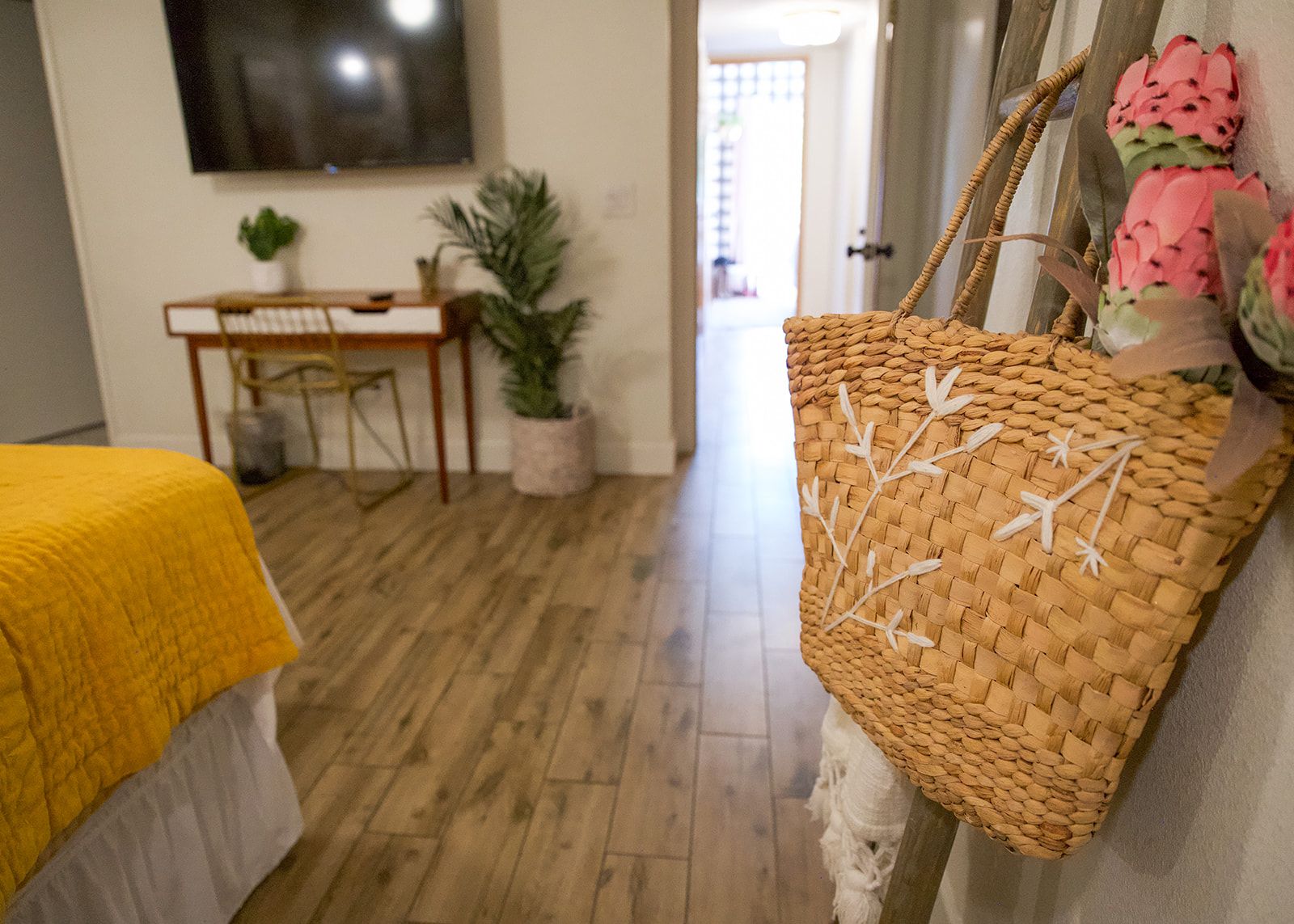 A room with a bed, a desk, a chair, a television, and a woven basket.
