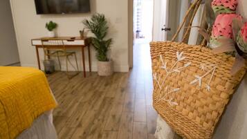 A room with a bed, a desk, a chair, a television, and a woven basket.