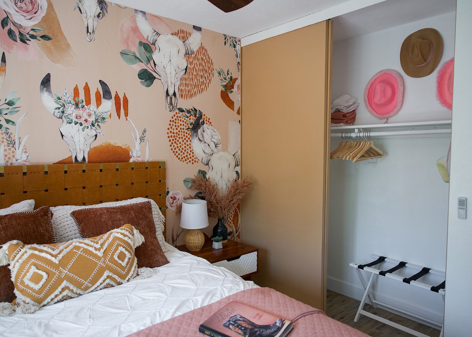 Une chambre à coucher comprenant un lit, une table de chevet, une lampe et un mur orné d’un motif floral et animal.