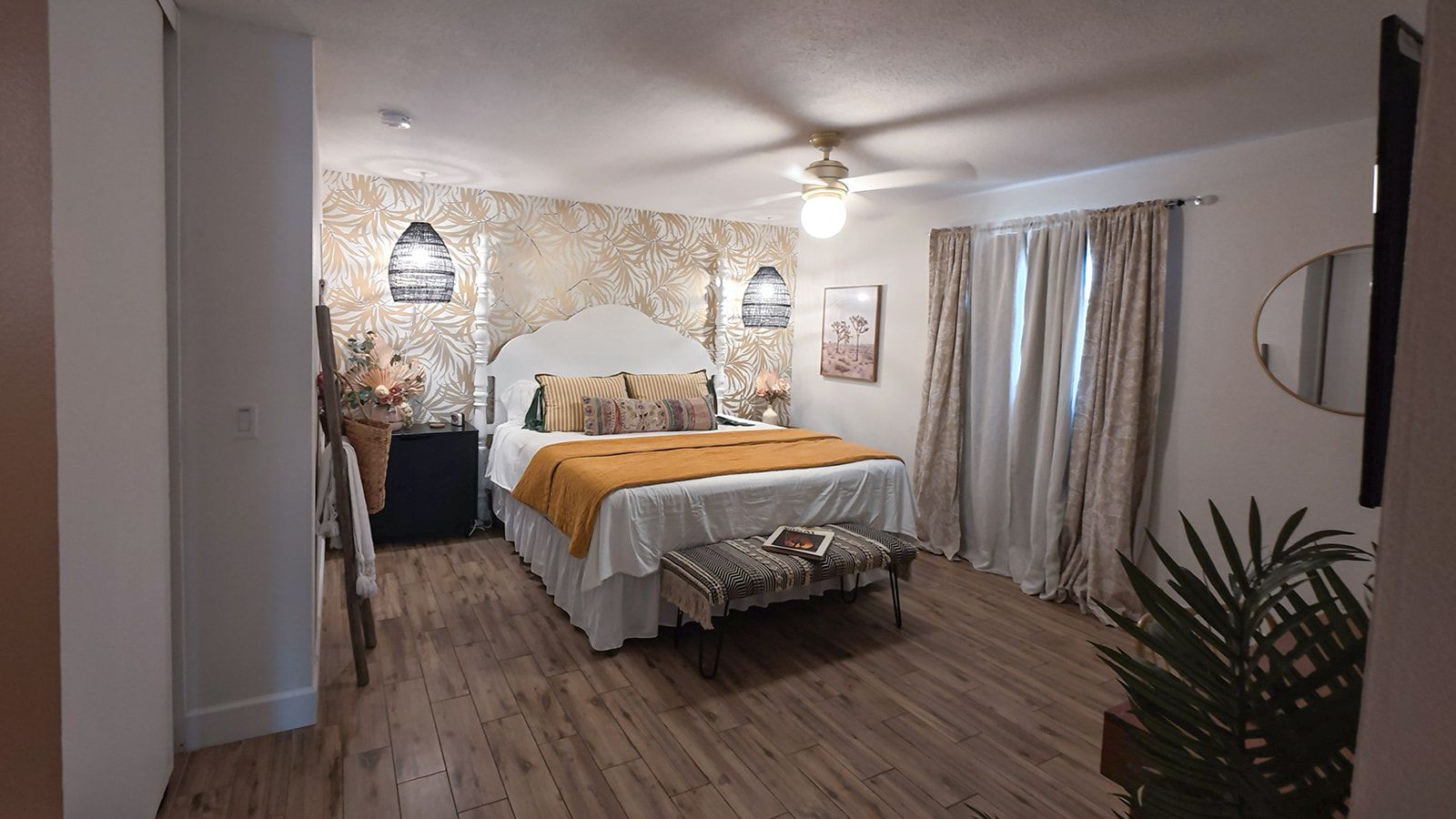 A bedroom with a bed, bedside tables, a bench, a ceiling fan, and a potted plant.