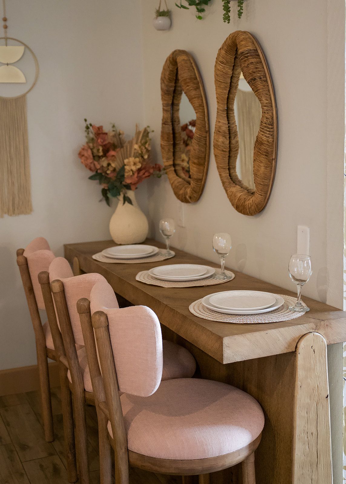 A wooden dining table with a vase of flowers and two mirrors on the wall.