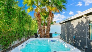A hot tub in a backyard with a pool, surrounded by palm trees and a house.