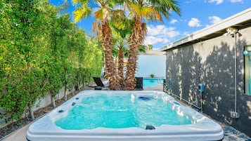 A hot tub in a backyard with a pool, surrounded by palm trees and a house.