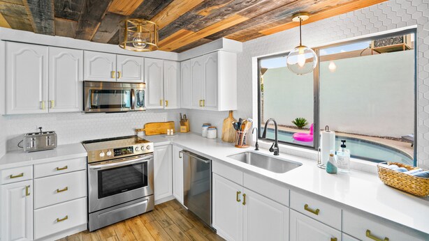 A modern kitchen with white cabinetry, stainless steel appliances, and a wooden ceiling.