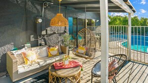 A covered outdoor seating area with wicker furniture, a hanging orange light fixture, and a view of a pool.