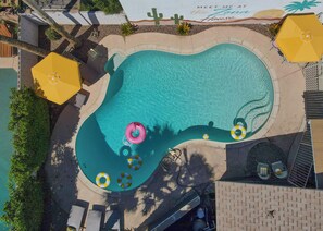 Vue aérienne d’une piscine à bord incurvé, entourée de chaises longues et de parasols.