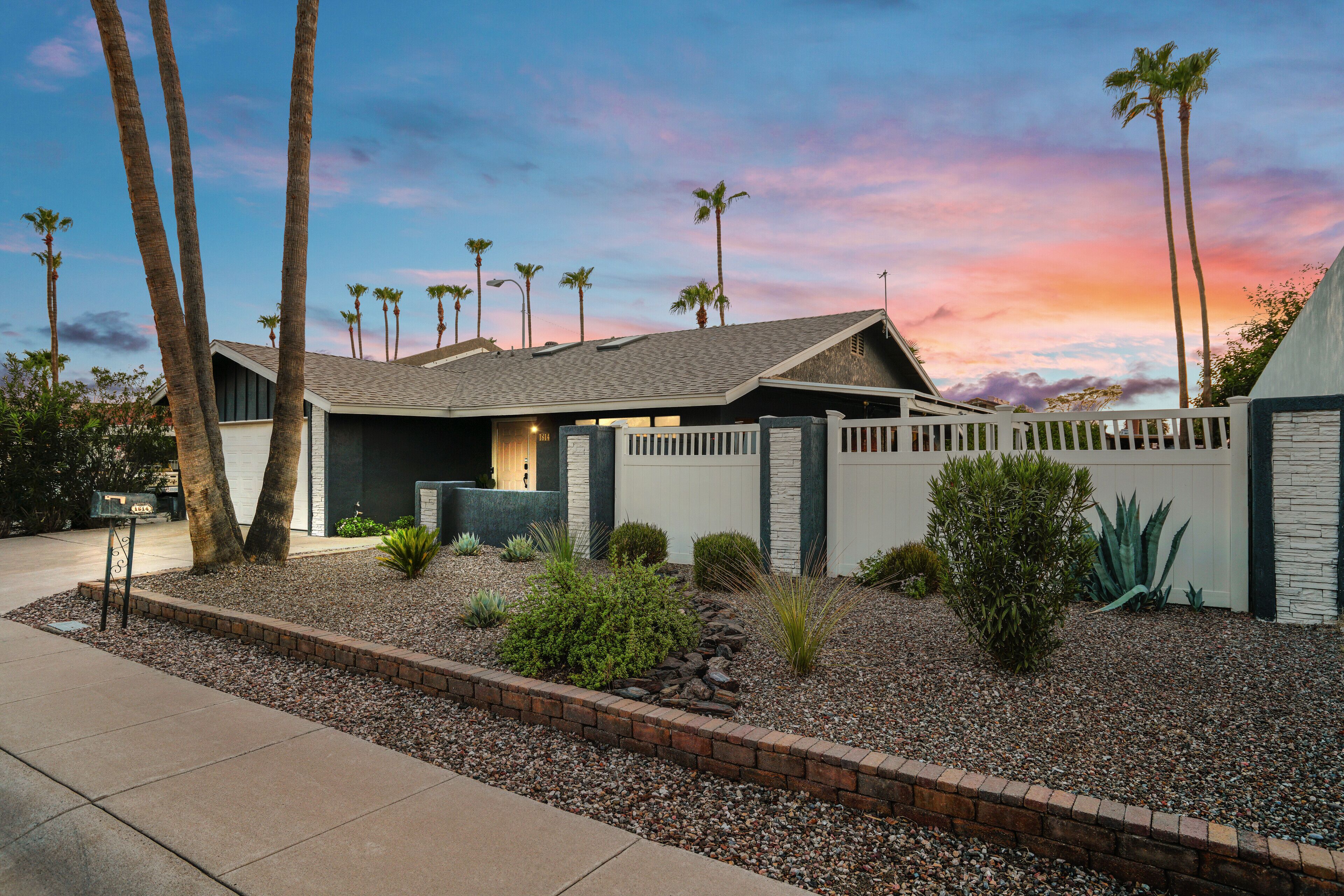A modern house with a sloped roof, a fenced backyard, and palm trees.