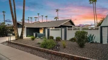 A modern house with a sloped roof, a fenced backyard, and palm trees.