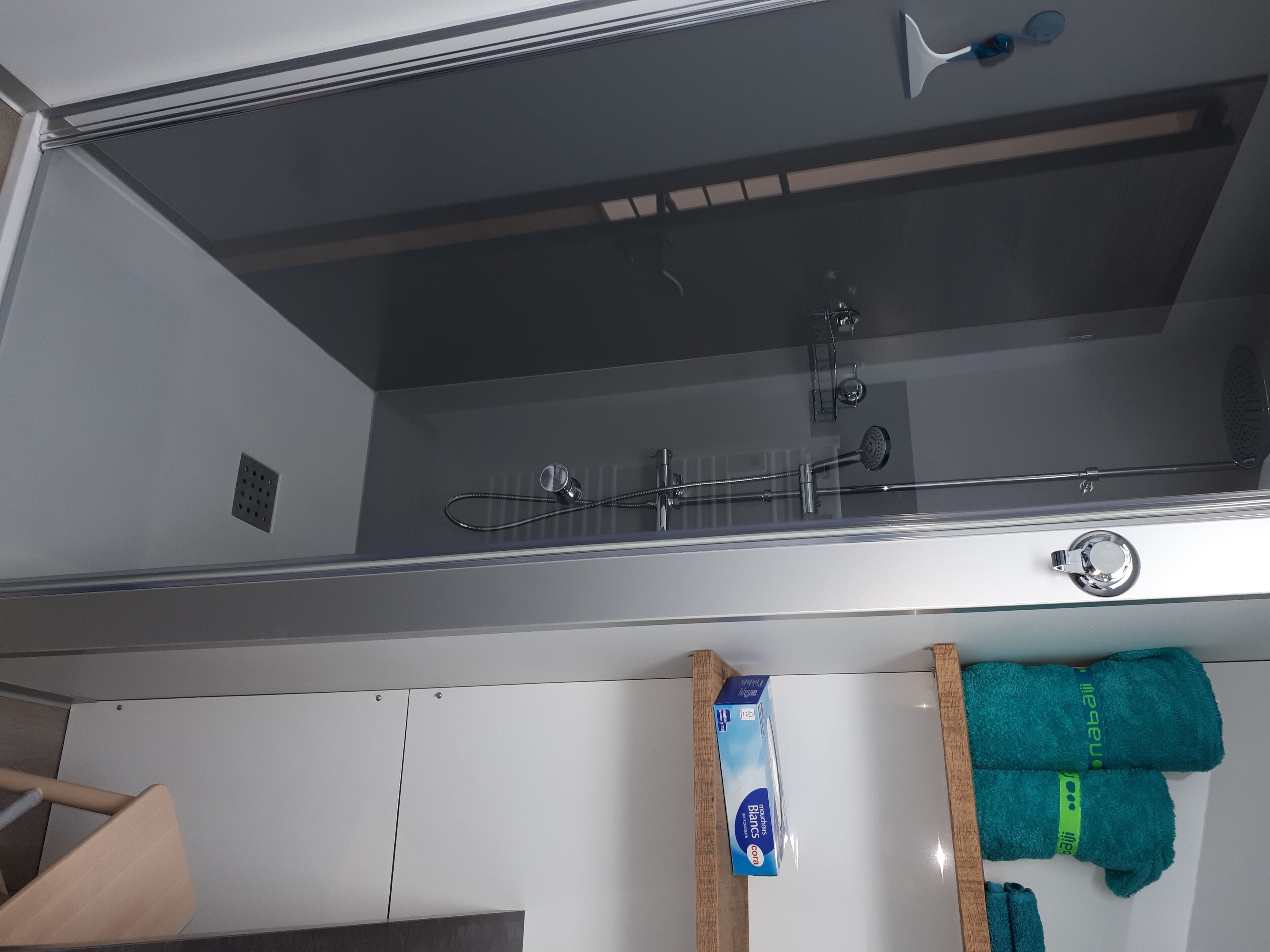 Une salle de bain avec une douche, un porte-serviettes avec des serviettes et une boîte contenant des articles de toilette.