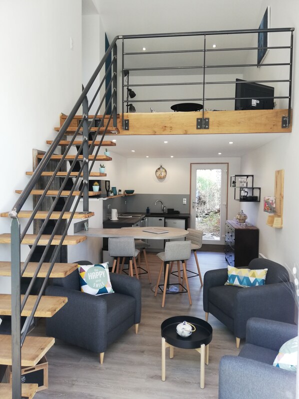 A modern loft apartment with a loft bed, a kitchen, a dining area, and a living room with two sofas and a coffee table.