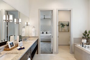 A modern bathroom with a large mirror, a granite countertop, a bathtub, and a shower area. - Arcadia #37 (Ivins)