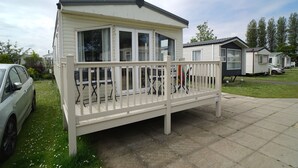 A single-story mobile home with a balcony, a car parked in front, and a grassy area. - Cozy Hunstanton Caravan Sleeps 8 Pets go Free (Hunstanton)