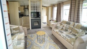 A compact living space with a sofa, a coffee table, a TV, and a kitchen area. - Cozy Hunstanton Caravan Sleeps 8 Pets go Free (Hunstanton)