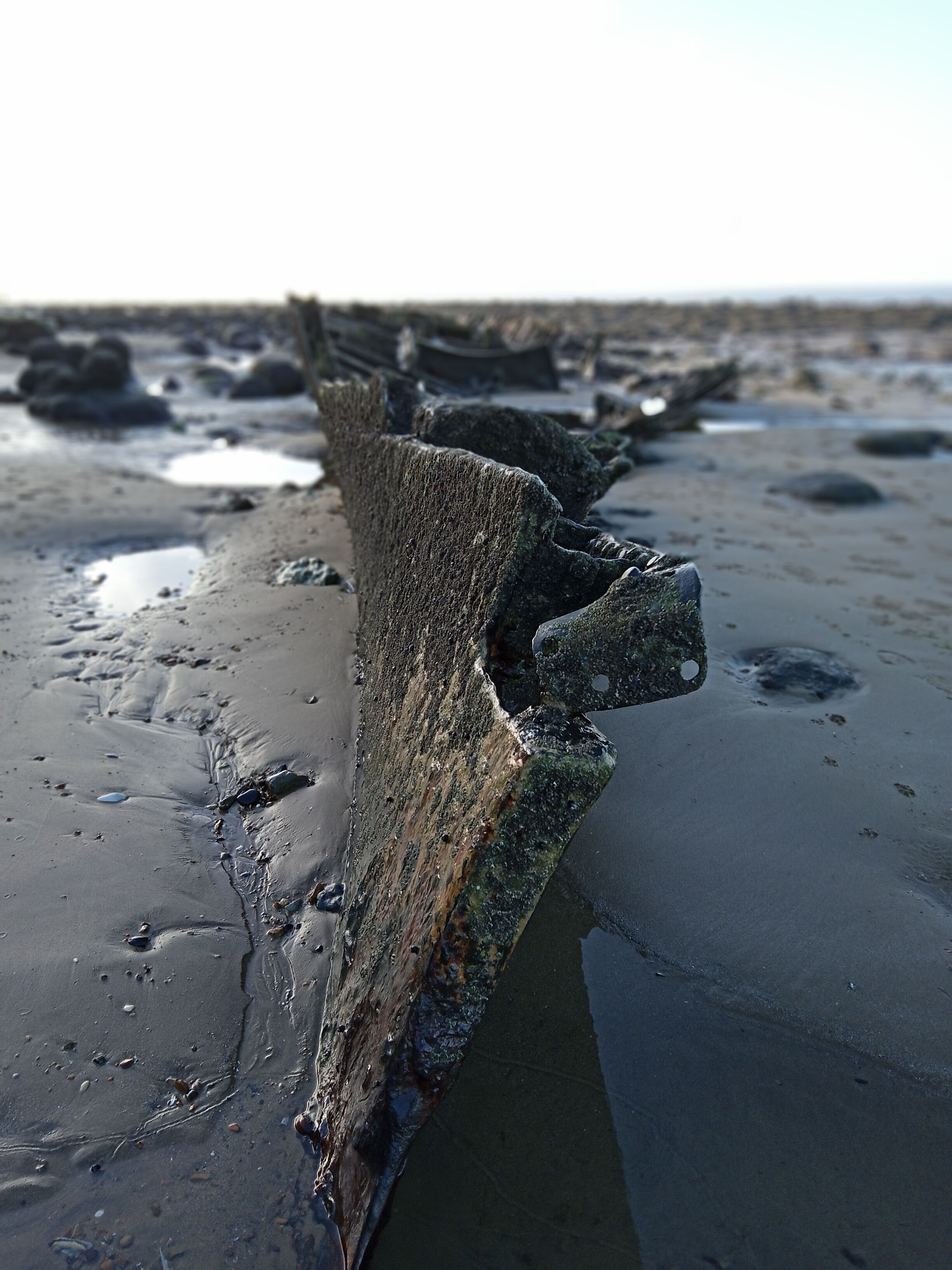 A large, weathered rock formation on a beach with wet sand and scattered pebbles.