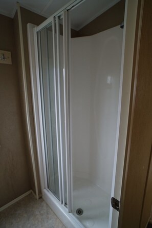 A walk-in shower with a glass door, a white tiled floor, and beige walls.