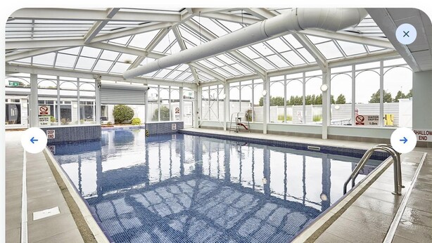 An indoor swimming pool with a glass ceiling, clear water, and safety signs indicating water depth. - Cozy Hunstanton Caravan Sleeps 8 Pets go Free (Hunstanton)