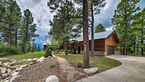 Une cabane en rondins avec un chemin de pierre menant à l’entrée, entourée de pins et bordée d’un mur de soutènement en pierre.
