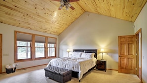 Une chambre avec un plafond en pente, un grand lit, deux lampes de chevet, une porte en bois et une fenêtre avec des stores.