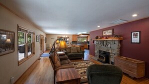A spacious living room with a fireplace, wooden furniture, and large windows. - Scenic Wonders Apple Tree Home 3 Br (Yosemite National Park)