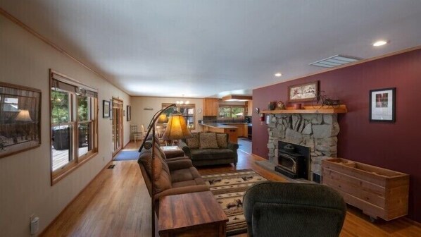 A spacious living room with a fireplace, wooden furniture, and large windows.