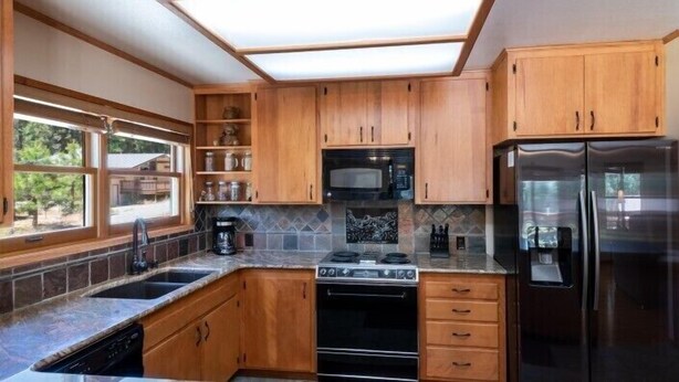 Une cuisine avec des meubles de rangement en bois, une cuisinière noire, un four à micro-ondes et un réfrigérateur.