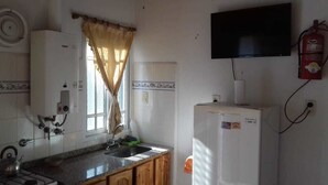 A kitchen with a gas stove, a sink, a refrigerator, a television mounted on the wall, and a fire extinguisher. - Aitue Departamentos (Colon)