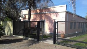 A gated entrance with a metal fence, a paved pathway, and a building with a pink facade in the background. - Aitue Departamentos (Colon)