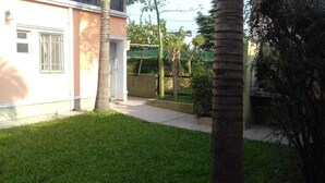 A residential area with a well-maintained lawn, a palm tree, and a house with a window and a door. - Aitue Departamentos (Colon)