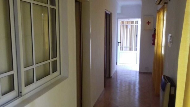A hallway with a window, a door, and a fire extinguisher on the wall. - Aitue Departamentos (Colon)