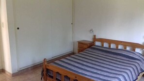 A small, single-bed room with a wooden headboard, a bedside table, and a striped bedspread. - Aitue Departamentos (Colon)