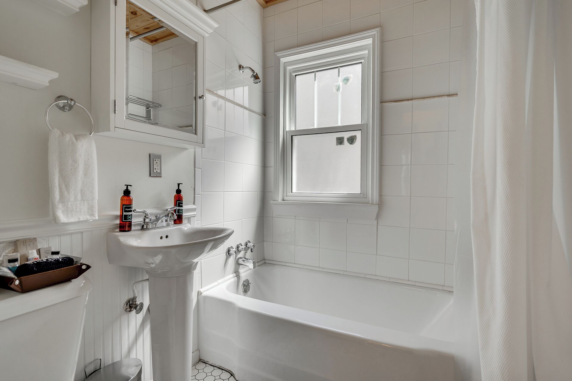 A bathroom with a white sink, a bathtub, a window, and a towel rack.