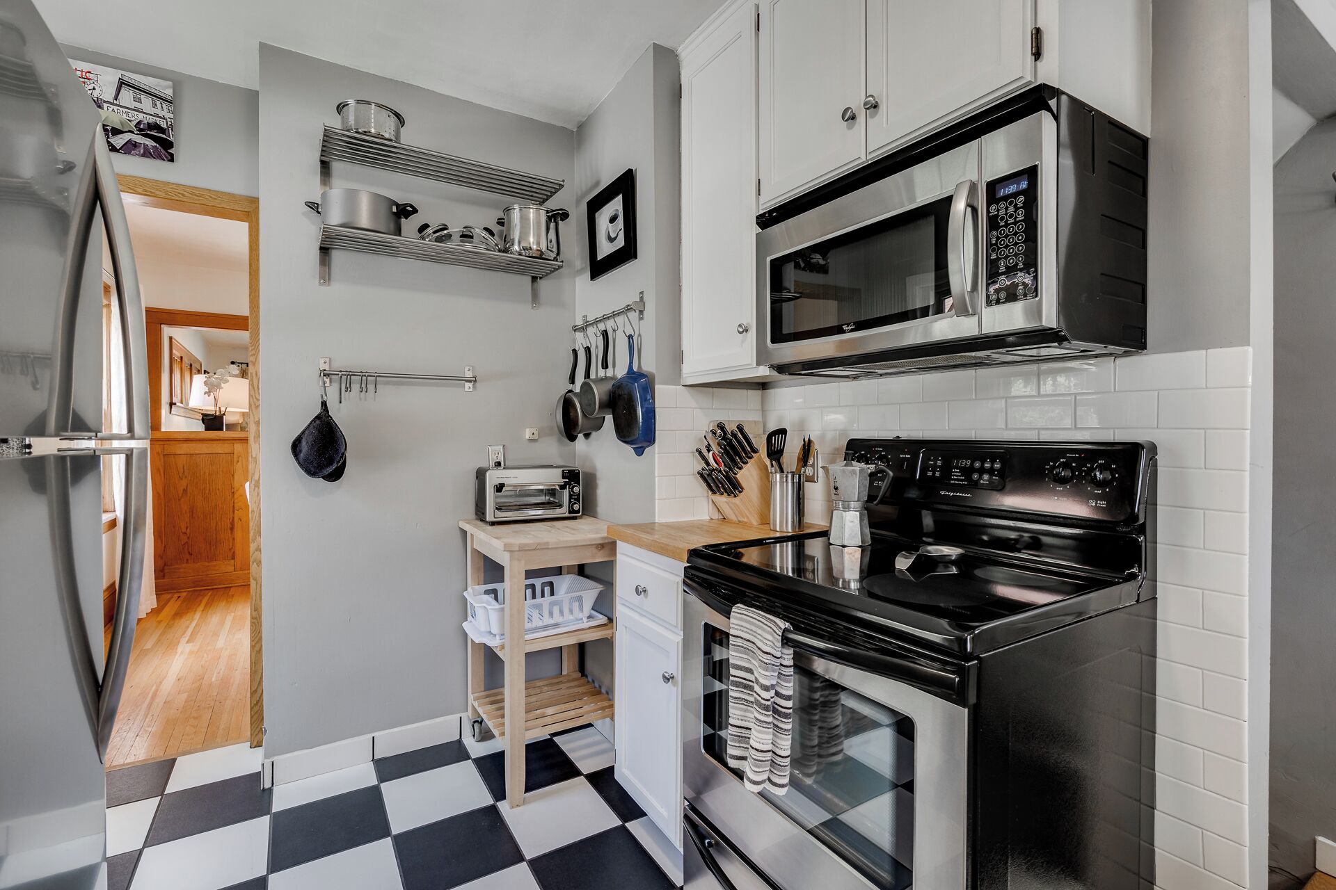 A compact kitchen with a microwave, oven, and toaster. There are shelves above the counter holding pots and pans.