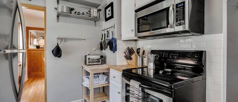 A compact kitchen with a microwave, oven, and toaster. There are shelves above the counter holding pots and pans.