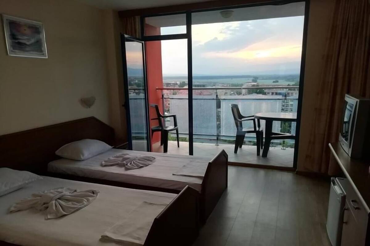 A hotel room with two beds, a balcony with a table and chairs, and a TV.