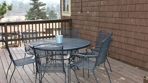 A wooden deck with a metal table and chairs, a metal bucket, and a sign reading "Ponderosa Ranch House." - Charming Two bedroom Cabin, Dog Friendly close to National Park (Estes Park)