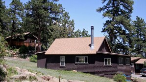 A wooden cabin with a chimney, surrounded by trees and rocks. - Charming Two bedroom Cabin, Dog Friendly close to National Park (Estes Park)