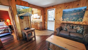 A cozy cabin interior with a wooden floor, a sofa, a small table, a kitchen area, and a door leading outside. - Charming Two bedroom Cabin, Dog Friendly close to National Park (Estes Park)
