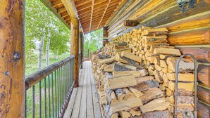 A wooden log cabin with a covered porch, a metal railing, and a stack of firewood. - Log Home on 40-Acre Crested Butte Ranch (Crested Butte)