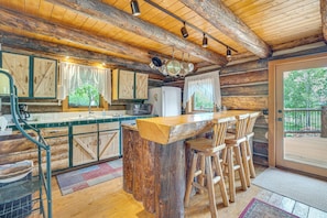 A rustic kitchen with wooden cabinets, a bar area with stools, and a large window.