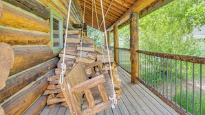 A log cabin with a porch, wooden logs stacked on the side, and a swing hanging from the ceiling. - Log Home on 40-Acre Crested Butte Ranch (Crested Butte)
