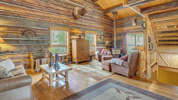 A log cabin interior with a wooden ceiling, a fireplace, a wooden table, and a sofa. - Log Home on 40-Acre Crested Butte Ranch (Crested Butte)