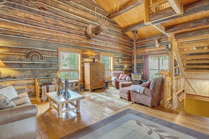 A log cabin interior with a wooden ceiling, a fireplace, a wooden table, and a sofa.