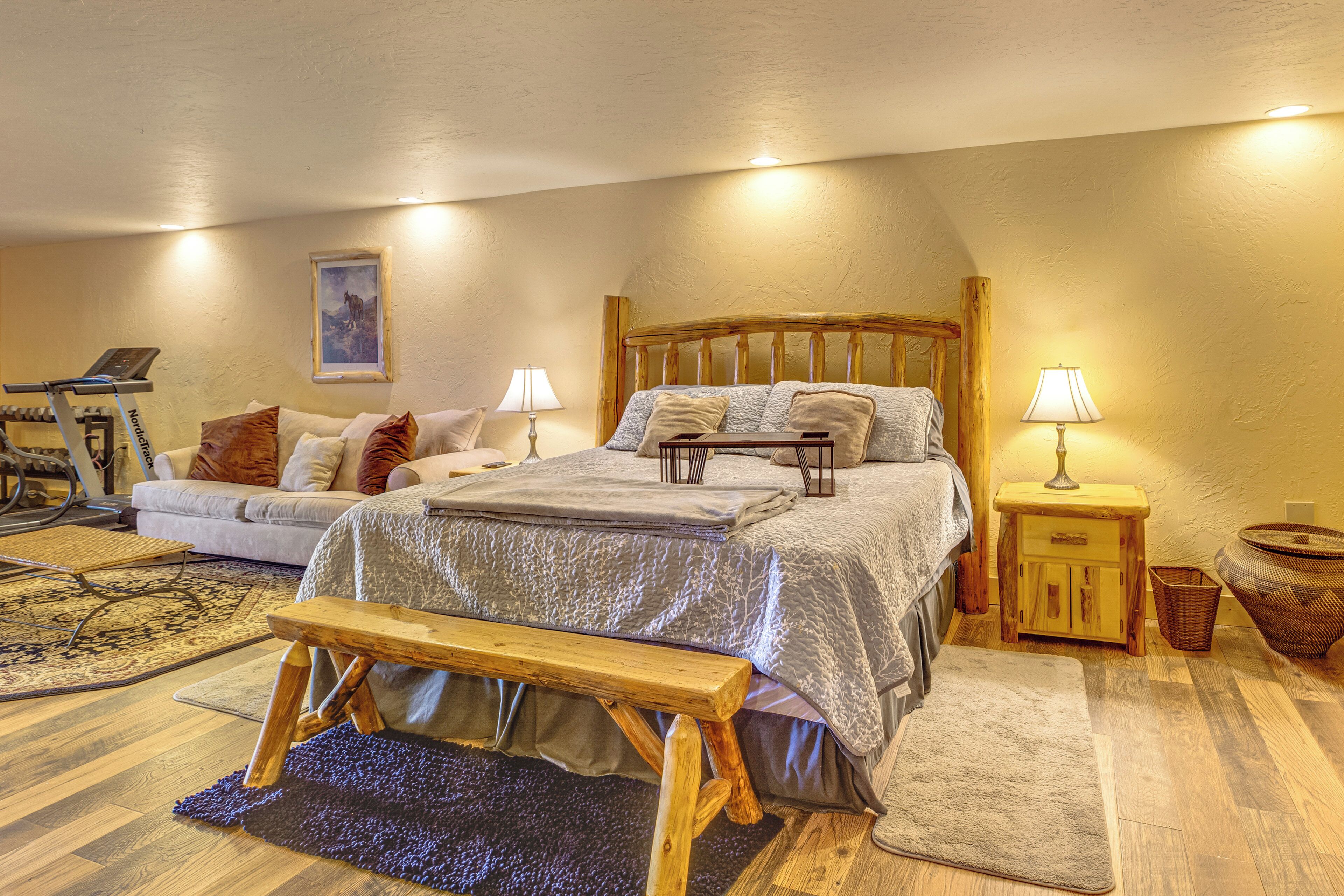 A bedroom with a bed, bedside tables, a bench, a treadmill, and a yoga mat.