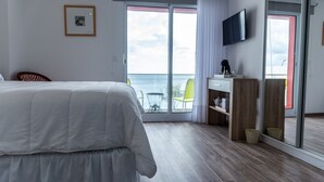 Habitación de hotel moderna con una cama grande, un escritorio, una silla, un televisor y un balcón con vistas al mar.
