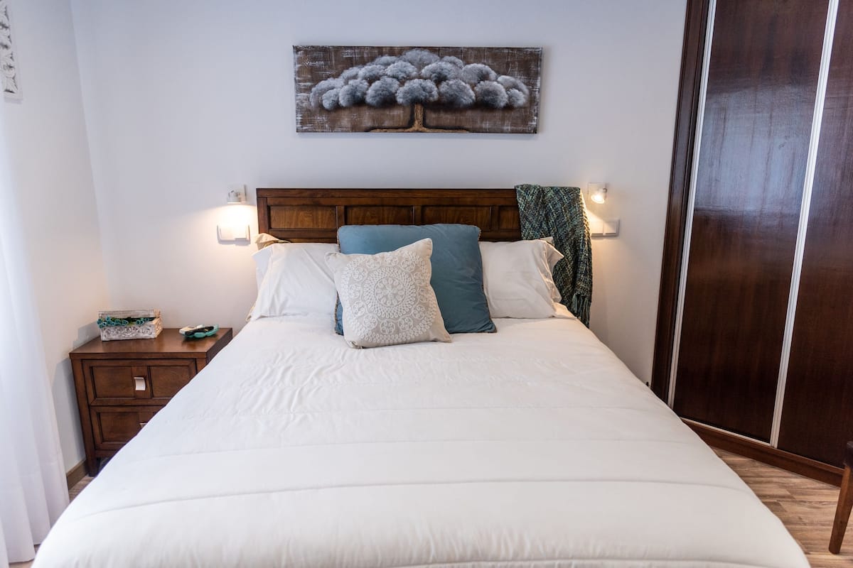 A neatly made bed with a wooden headboard, a nightstand with a lamp, and a wall-mounted artwork above the bed.