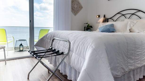 Un dormitorio con cama, una silla, una planta y vistas al mar.