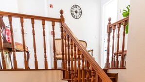 Una escalera de madera con barandilla, un extintor, un cuadro enmarco, un televisor, una alfombra estampada y una silla.