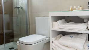 Un baño moderno con cabina de ducha de vidrio, inodoro blanco y tocador con toallas dobladas con esmero.